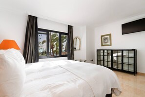 Ein Hotelzimmer mit Bett, einem Fenster mit Vorhängen, einem Nachttisch, einem an der Wand montierten Fernseher und einem Schrank mit Glastüren.