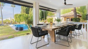 A modern dining area with a pool view, large windows, and a ceiling fan. - 3310 Villa Flores (Marbella)
