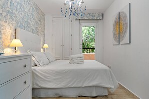 A bedroom with a bed, two bedside lamps, a dresser, a window with a view, and a wall-mounted artwork. - 3316 Casa Jacaranda (Marbella)