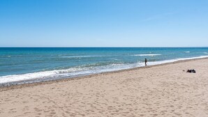 En strand med sand, en person som går och en klar himmel.