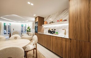A modern kitchen with wooden cabinetry, a marble countertop, and a dining area with a round table and chairs. - NESTLED IN THE VIBRANT & HISTORIC SAINT-GERMAIN WITH PRIVATE TERRACE – 3 BEDROOM (Paris)