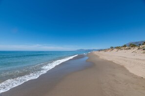 Ein Strand mit klarem Himmel, ruhiger See und fernen Bergen.