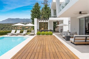 Ein Poolbereich im modernen Stil mit Holzterrasse, Liegestühlen und Sonnenschirmen.