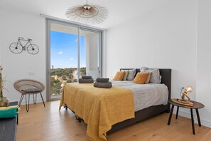 Ein Schlafzimmer mit Bett, Stuhl, einem kleinen Tisch und Blick durch ein großes Fenster.