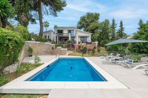 A swimming pool with a person swimming, surrounded by lounge chairs and a house in the background. - 3305 Carib Playa (Marbella)