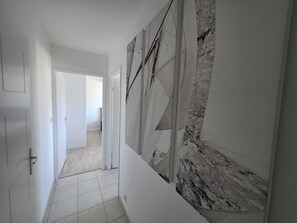 Un passadís amb sòl de rajoles, parets blanques i una porta que dona a una altra habitació.