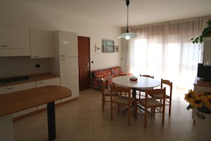 A kitchen with a dining table, chairs, and a sofa. - Comfortable sea View Stay (Lignano Sabbiadoro)