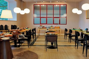 A dining area with multiple tables and chairs, a large window with red frames, and hanging spherical light fixtures. - Barberini 16 Boutique Hotel (Rome)