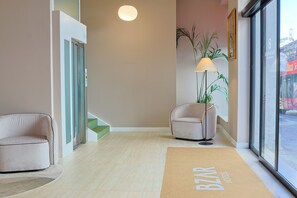 A hotel lobby with a reception desk, a sofa, a lamp, a plant, and a large window. - Barberini 16 Boutique Hotel (Rome)