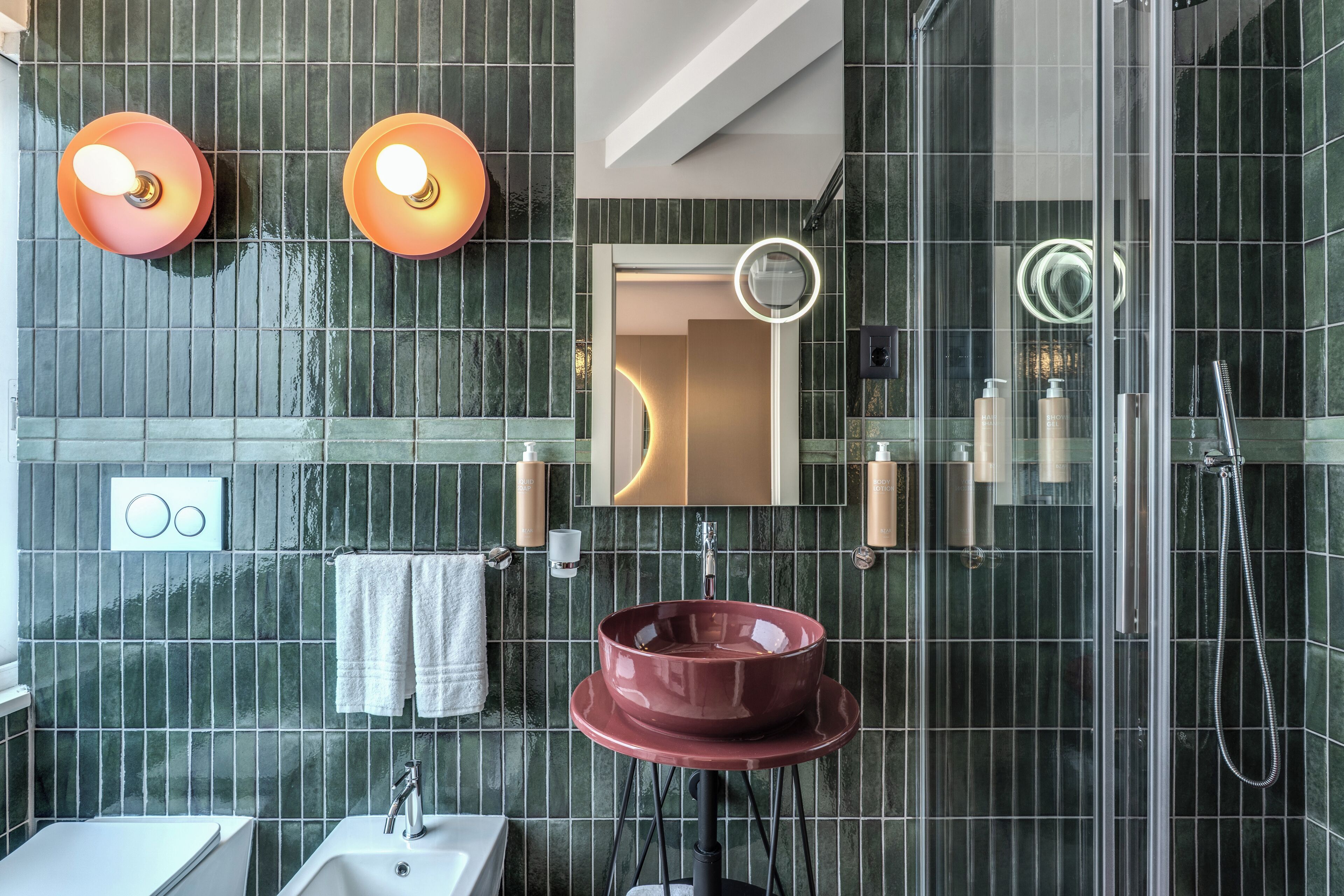 Une salle de bain moderne avec une douche à parois de verre, un lavabo rond et deux appliques murales.