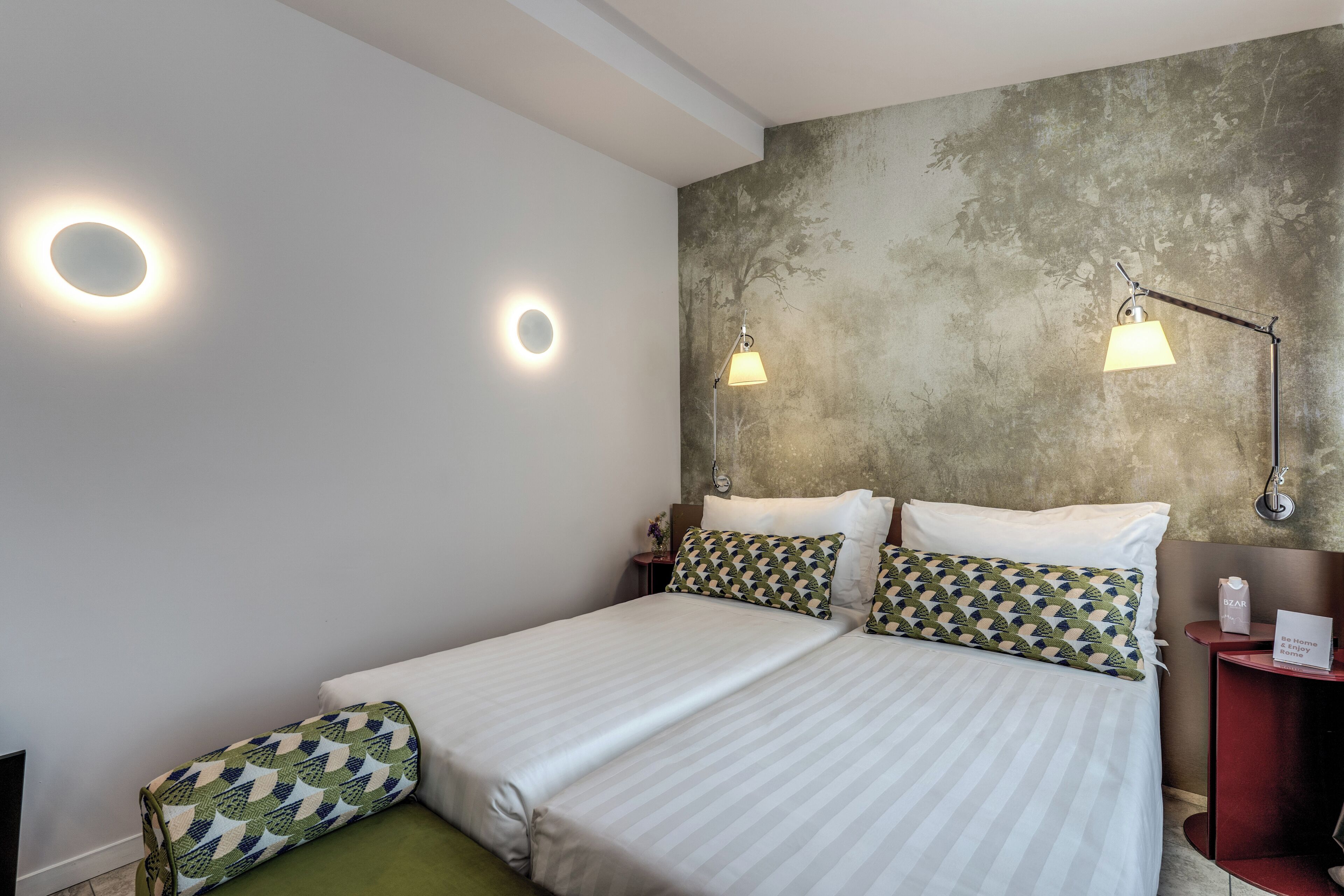 A hotel room with a large bed, two bedside lamps, a nightstand, and a green sofa.