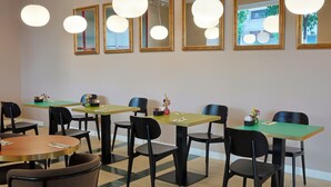 A dining area with multiple tables and chairs, a green and yellow color scheme, and large mirrors on the wall. - Barberini 16 Boutique Hotel (Rome)