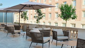 Una terraza en la azotea con mobiliario de mimbre, sombrillas y vistas a un edificio.