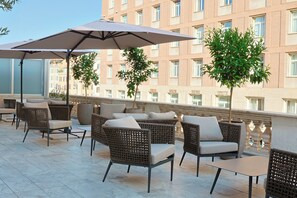 Een terras op het dak met rieten meubels, parasols en uitzicht op een gebouw.