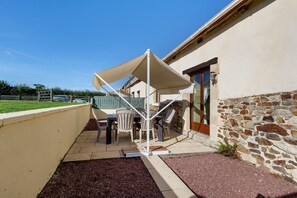 An outdoor patio area with a table and chairs, a stone wall, and a clear sky. - Puddle-duck Cottage – La Mare Chappey, children welcome, heated pool (Néhou)
