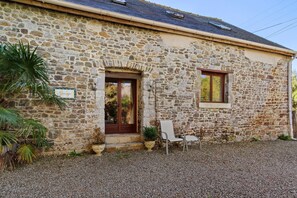 A stone building with a gravel driveway, a wooden door, and a window. - Gîte Grange – La Mare Chappey, child-friendly, heated pool (Néhou)