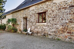 A stone building with a gravel driveway, a wooden door, and a window with a wooden frame. - Gîte Grange – La Mare Chappey, child-friendly, heated pool (Néhou)