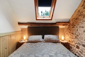 Une chambre avec un plafond en pente, un puits de lumière, un lit avec une literie à motifs floraux et deux lampes de chevet.