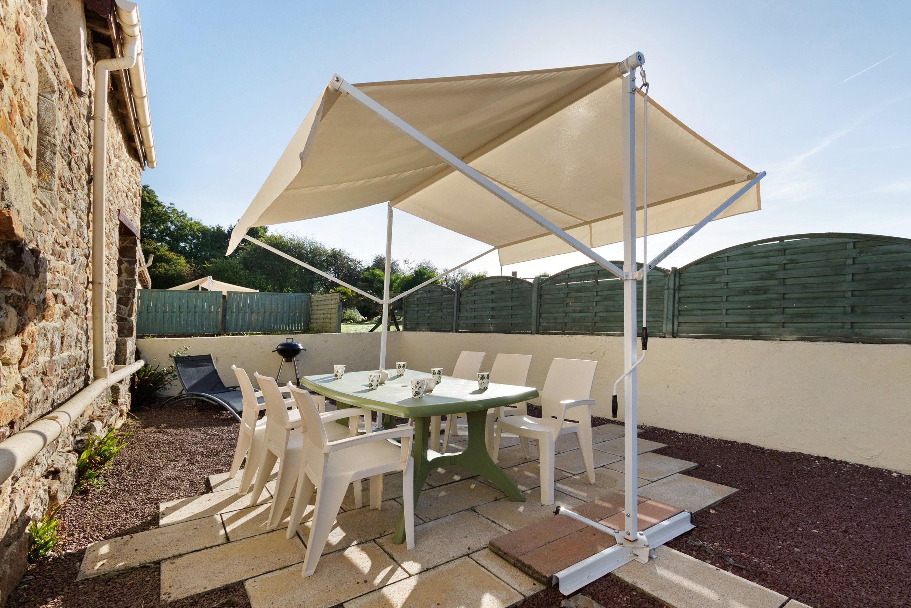 Una terrazza esterna con tavolo e sedie, un barbecue e un'ampia tettoia.