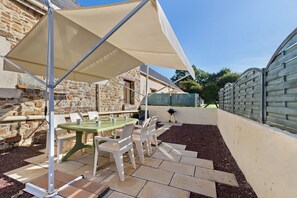 An outdoor patio with a table and chairs, a barbecue grill, and a stone wall. - Gîte Grange – La Mare Chappey, child-friendly, heated pool (Néhou)