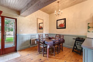 Un comedor con mesa de madera dispuesta para cuatro, una araña y vistas al exterior a través de una puerta.