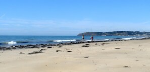Ein Strand mit felsiger Küste, ruhigem Meer und einer entfernten Hügelkette mit Gebäuden.
