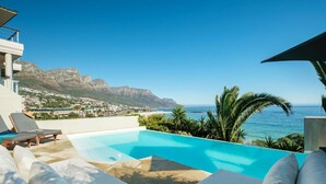 A pool with lounge chairs, a view of the ocean, and mountains in the background. - Camps Bay 6bed w Ocean Views and Pool Villa Sevara (Cape Town)
