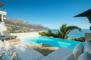 A pool with lounge chairs, a view of the ocean, and mountains in the background. - Camps Bay 6bed w Ocean Views and Pool Villa Sevara (Cape Town)