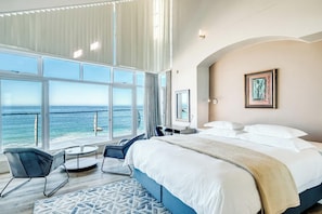 A bedroom with a large bed, a desk, a chair, and a view of the ocean. - Camps Bay 6bed w Ocean Views and Pool Villa Sevara (Cape Town)