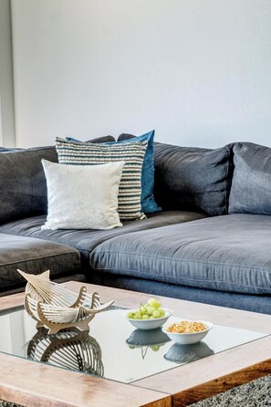 Een moderne woonkamer met een grijze bank, een glazen salontafel en decoratieve objecten.