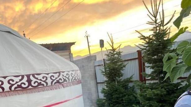 Een barbecue met vlees dat gebakken wordt, een tent met decoratieve versieringen, en een persoon op de achtergrond.