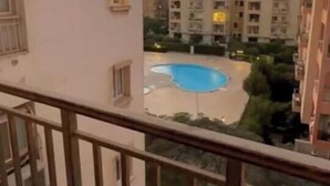 Edifício residencial com varanda com vista para uma piscina e edifícios altos vizinhos.