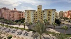 A multi-story residential building with balconies, a central tower, and a surrounding landscaped area with palm trees. - Stylish & Sunny 2BR Retreat – Spacious Living with Large Pool Access (Giza Governorate)