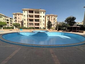 A swimming pool with a tiled deck, surrounded by multi-story residential buildings. - Stylish & Sunny 2BR Retreat – Spacious Living with Large Pool Access (Giza Governorate)