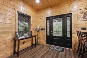 Een houten interieur met een zwarte deur, een bankje, een vaas en een welkomstmat.