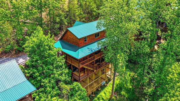 A multi-story wooden cabin with a green roof, surrounded by dense forest. - Minutes from Pigeon Forge - NEW 5 Bed/5Bath Rental - Slps 12 (Pigeon Forge)