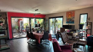 Un amplio salón con una mesa de comedor, asientos cómodos, una estantería y un gran ventanal con vistas al exterior.