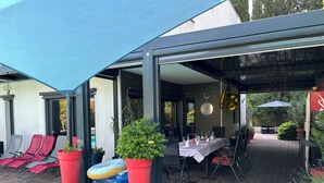 Un patio al aire libre con una zona de estar cubierta, una piscina y plantas en macetas.