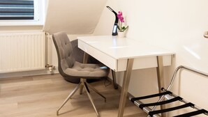 Een moderne, goed verlichte kamer met een wit bureau, een grijze stoel en een zwarte bankje. Er is een raam met zonwering en een radiator te zien.