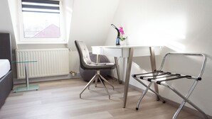 Een moderne, goed verlichte kamer met een wit bureau, een grijze bureaustoel, een metalen klapstoel en een radiator.