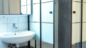 Een moderne badkamer met een douchecabine van glas, een witte wastafel en een donkere badkamerkast.