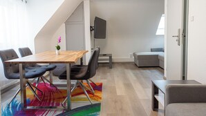 Een moderne woonkamer met een houten eettafel, grijze banken en een kleurrijk vloerkleed.