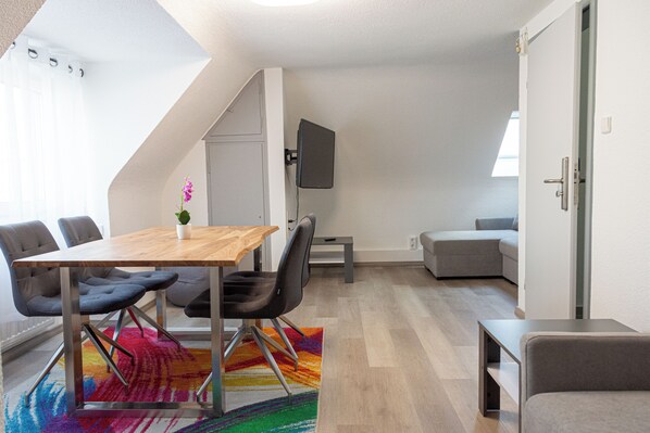 A modern living room with a wooden dining table, grey sofas, and a colorful rug.