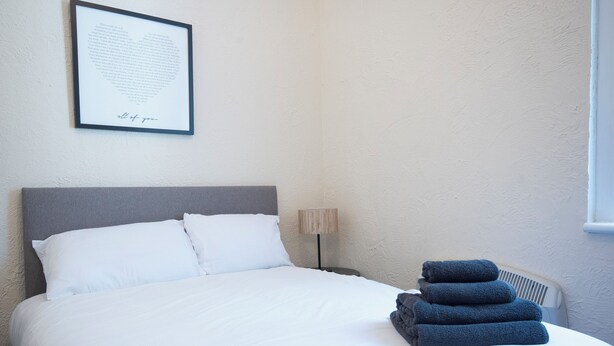 A neatly made bed with white linens and a stack of folded towels on the side. - St Andrews By Guestz (Lytham Saint Annes)