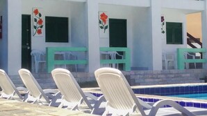 A poolside area with lounge chairs and a building with balconies and windows. - Pousada Suites de Porto (Ipojuca)