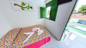 A room with a bed, a window with green shutters, a painting on the wall, and a view of a pool outside. - Pousada Suites de Porto (Ipojuca)