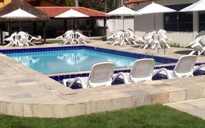 A swimming pool with lounge chairs and umbrellas, surrounded by a stone deck and grass. - Pousada Suites de Porto (Ipojuca)