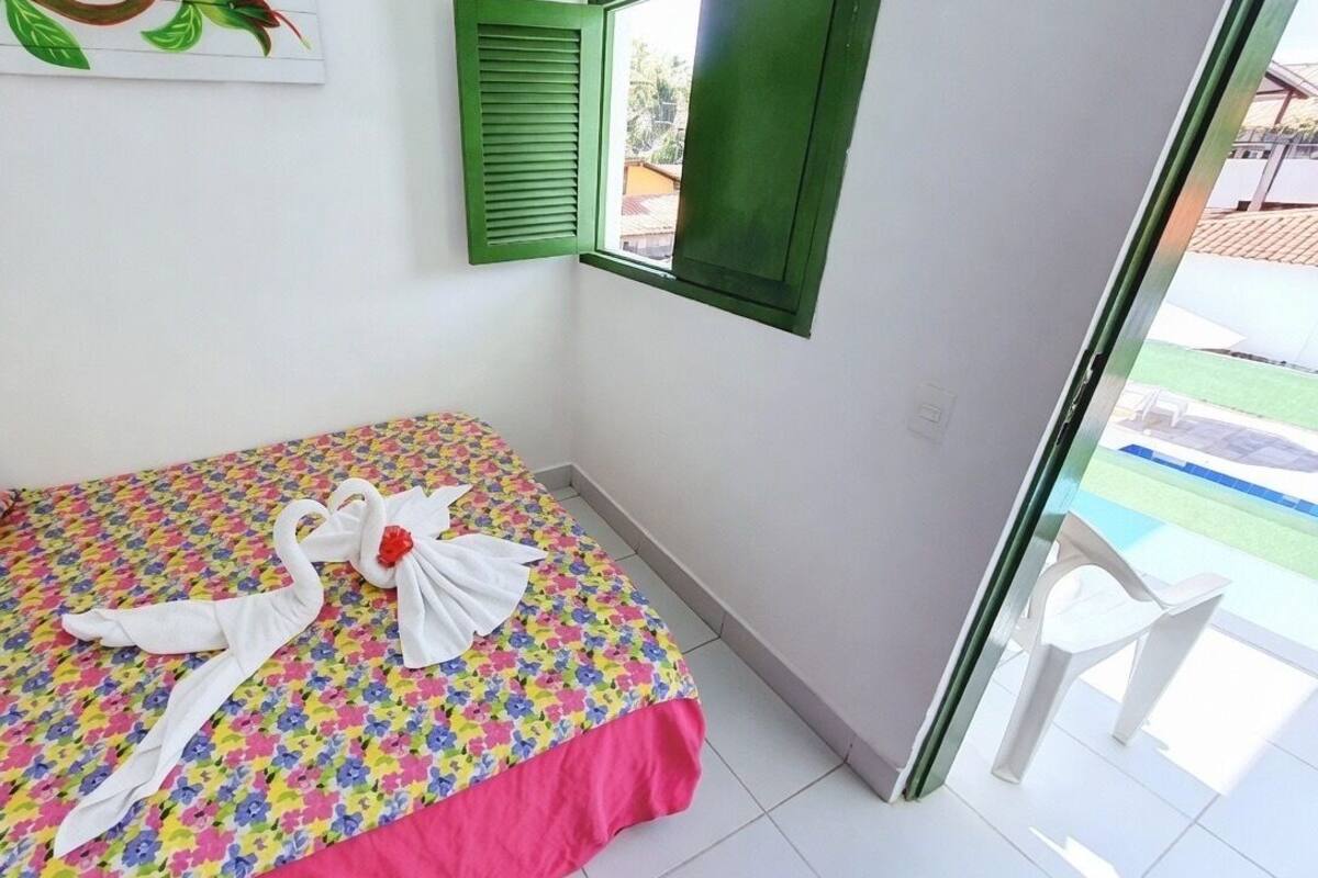 Habitación de hotel con cama, ventana con contraventanas verdes, vista a una piscina y un cuadro en la pared.