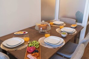 Una mesa de desayuno dispuesta con platos, vasos, una bandeja de fruta y un postre cubierto.