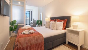 Ett modernt hotellrum med en stor säng, sängbord, en platt-TV och utsikt över staden.